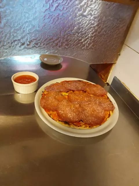 Pica s pikantno salamo na krožniku, ob njej pekoča omaka.